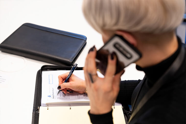 Close up of person holding a phone to their ear and taking notes on a notebook